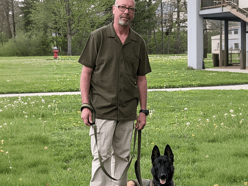 Man with a black dog on a leash outdoors.