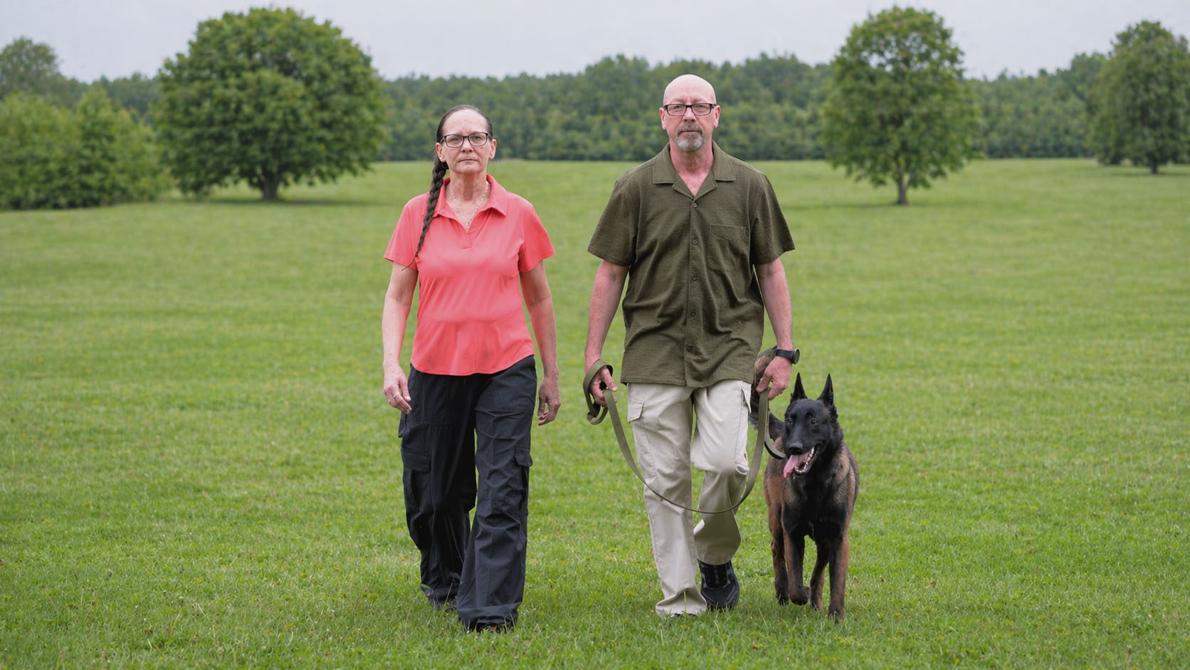 A couple walking their dog in a grassy park.