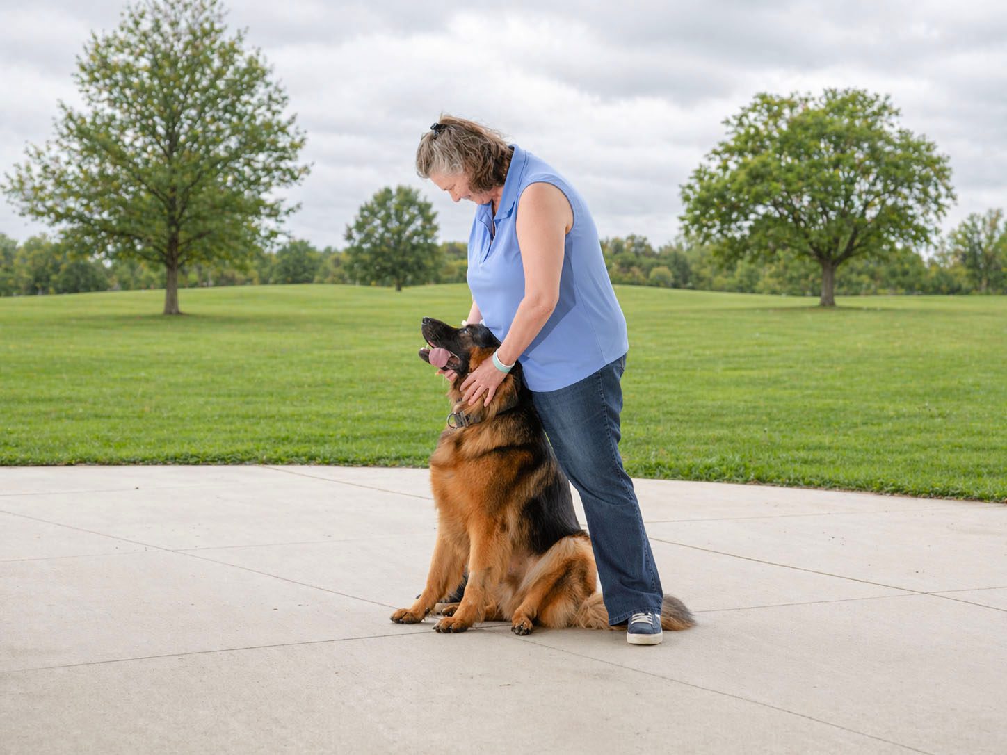 A woman affectionately hugging a German Shepherd dog outdoors.